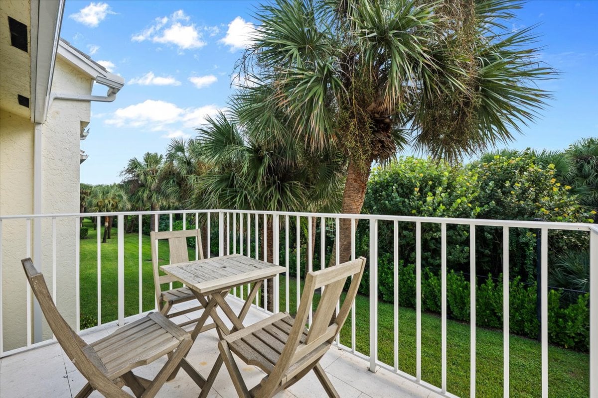 Condominium balcony with wooden table and chairs overlooking a palm-lined lawn.