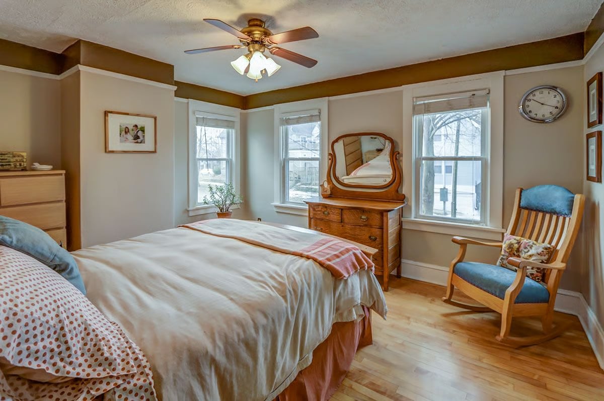 Furnished bedroom with a large bed, wooden dresser and mirror, and blue-cushioned rocking chair.