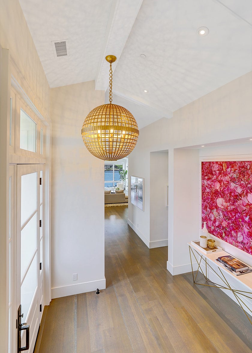 Entry hall with a gold globe pendant, wood floors, and vivid pink floral artwork.