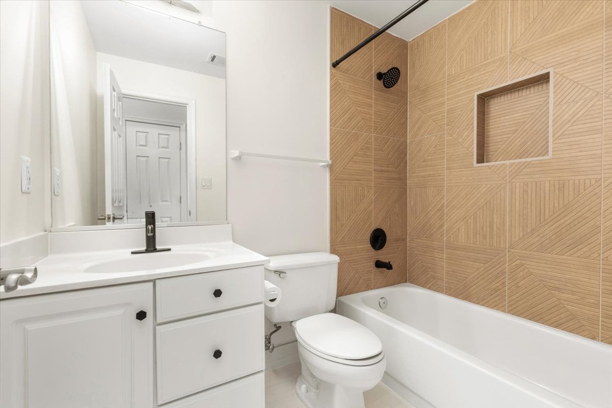 Bathroom with white vanity and bathtub, tan geometric tile surround, and black shower fixtures.