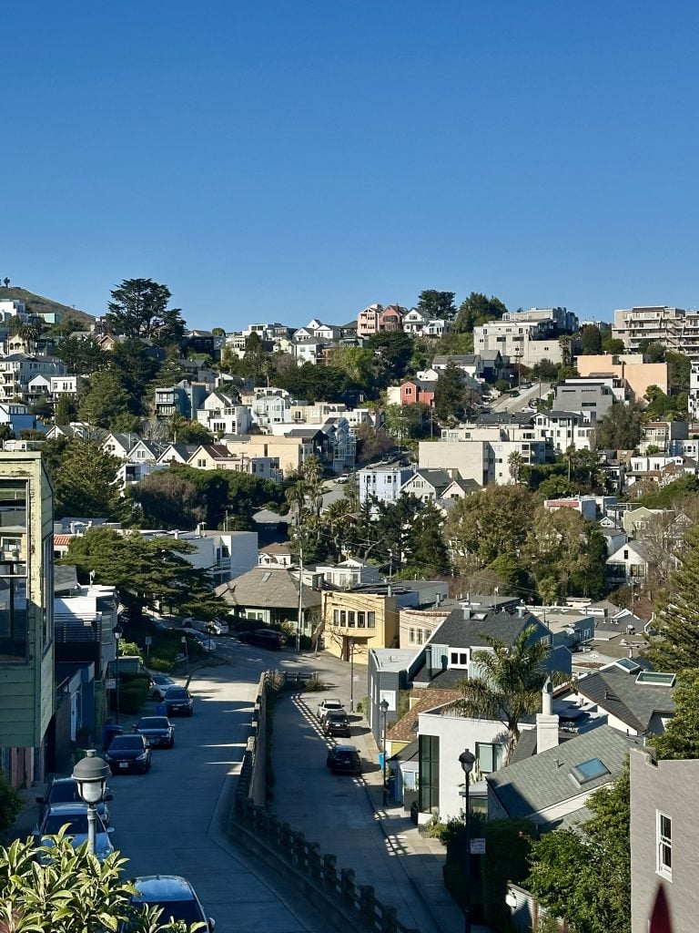 Hillside neighborhood of homes and apartment buildings above a quiet street.