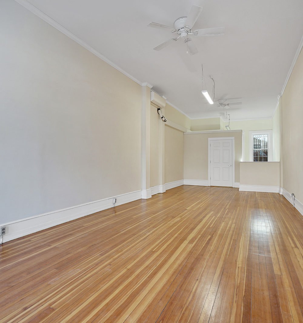 Vacant room with polished wood floors, ceiling fans, and a door and window at the far end.