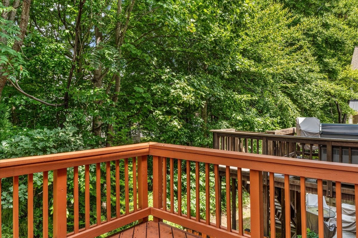 Wooden deck overlooking dense green trees, with a covered grill on the neighboring deck.
