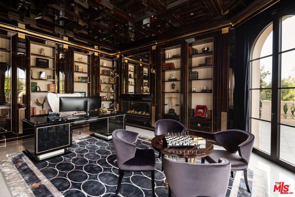 Furnished home office with dark wood shelves, a desk, and a chess table beside arched glass doors.