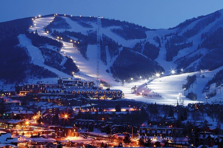 Snow-covered ski slopes above a warmly lit mountain village at dusk.
