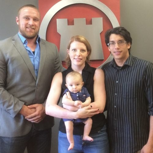 Three adults pose with a baby in front of a red-and-white wall emblem.