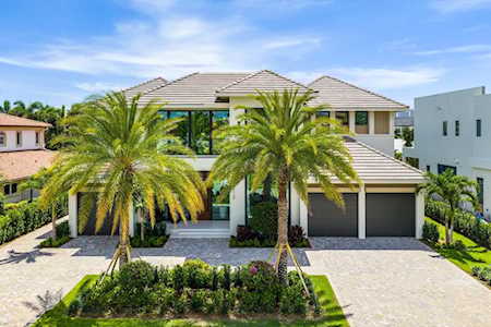 Modern two-story home with a two-car garage, palm trees, and a broad paved driveway.
