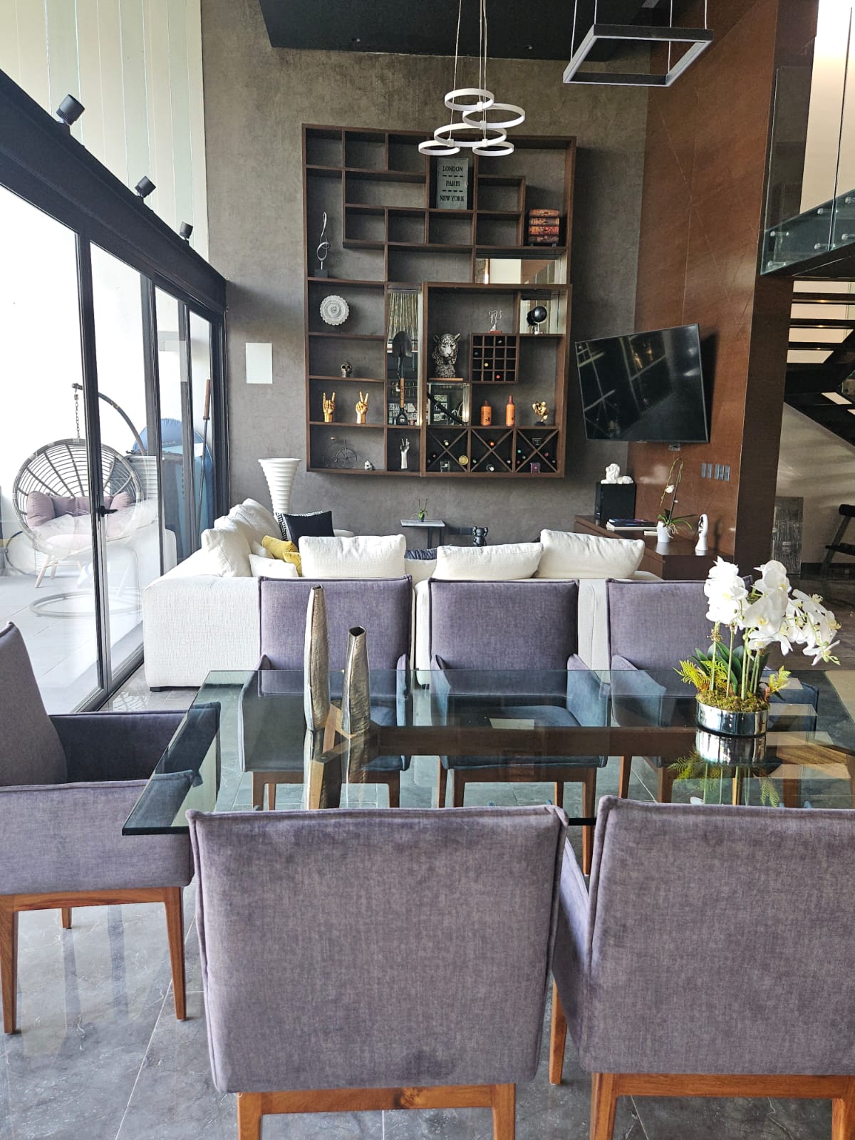 Living and dining room with a white sectional, built-in display shelving, and glass dining table.