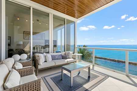 Oceanfront balcony with wicker seating and a glass railing overlooking turquoise water.