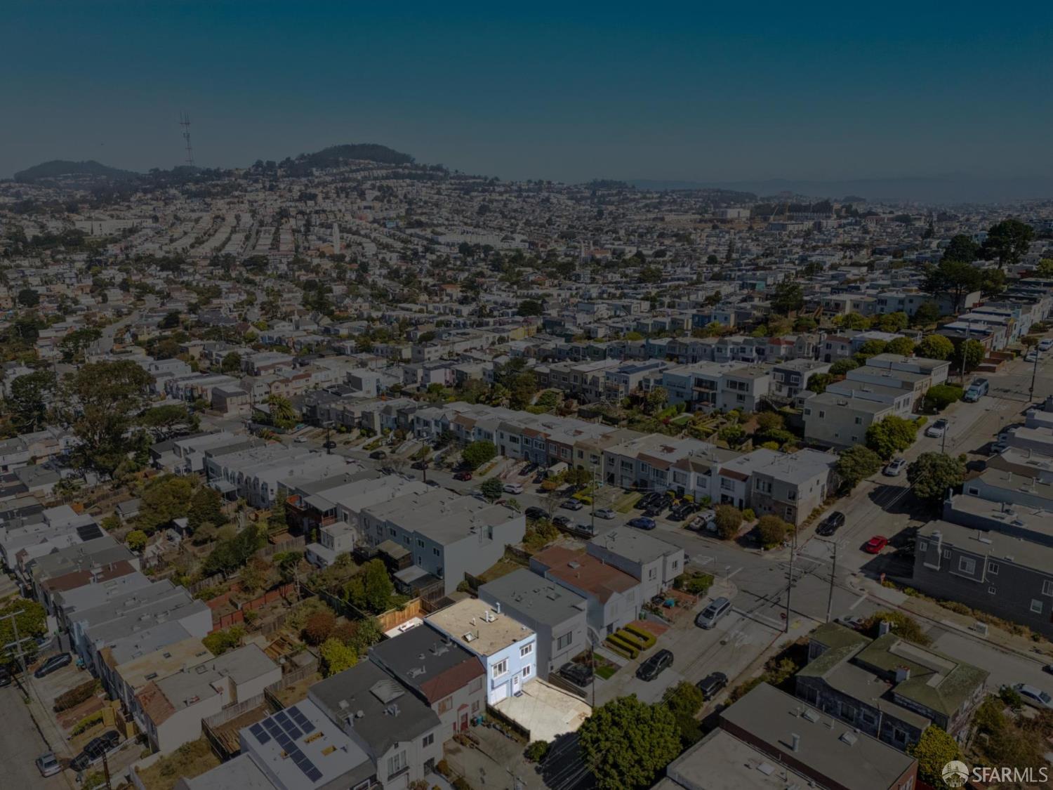 Aerial view of a dense neighborhood with rows of homes and distant hills.