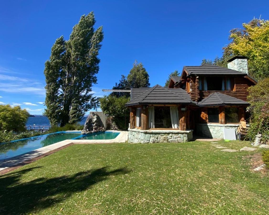 Log cabin home beside a lake, with a swimming pool and stone water feature.