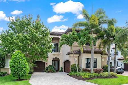 Two-story stucco home with arched entry, tiled roof, palms, and a curved driveway.