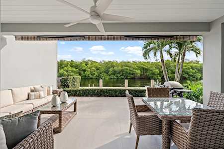 Covered patio with wicker seating and a glass-top dining table overlooking palm trees and greenery.
