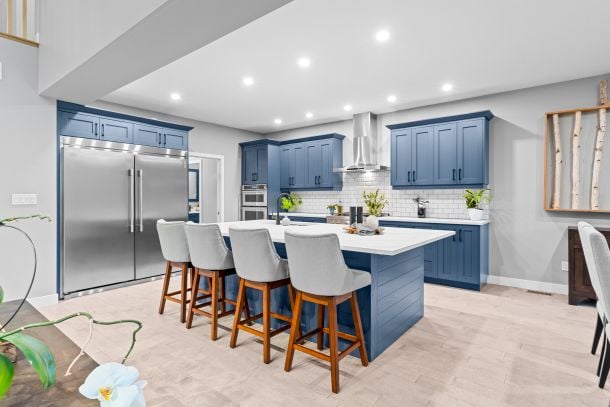 Modern kitchen with blue cabinets, a white island and seating, and stainless steel appliances.