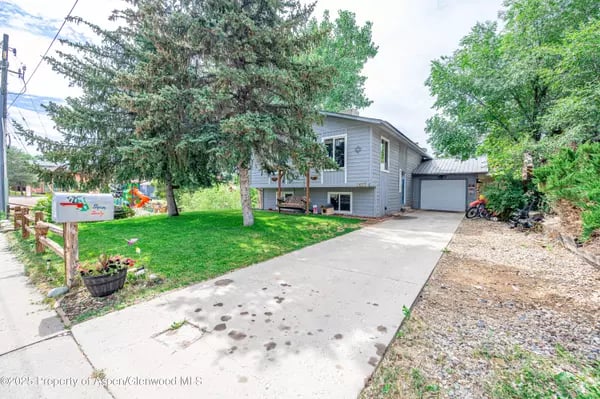 Gray two-story home with an attached garage, wide driveway, and mature trees.