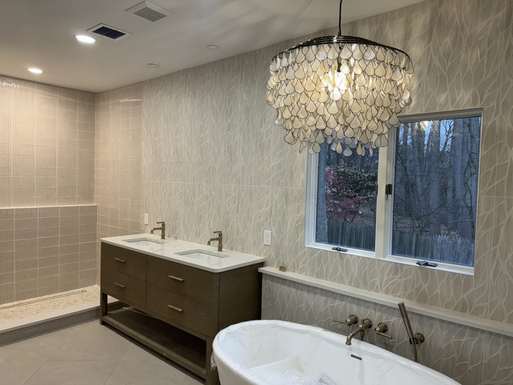 Luxury bathroom with a freestanding tub, double vanity, tiled shower, and sculptural chandelier.