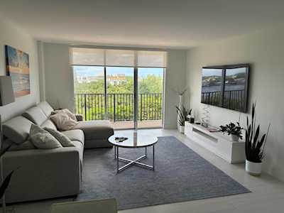 Living room with a gray sectional, round coffee table, and balcony doors overlooking trees.
