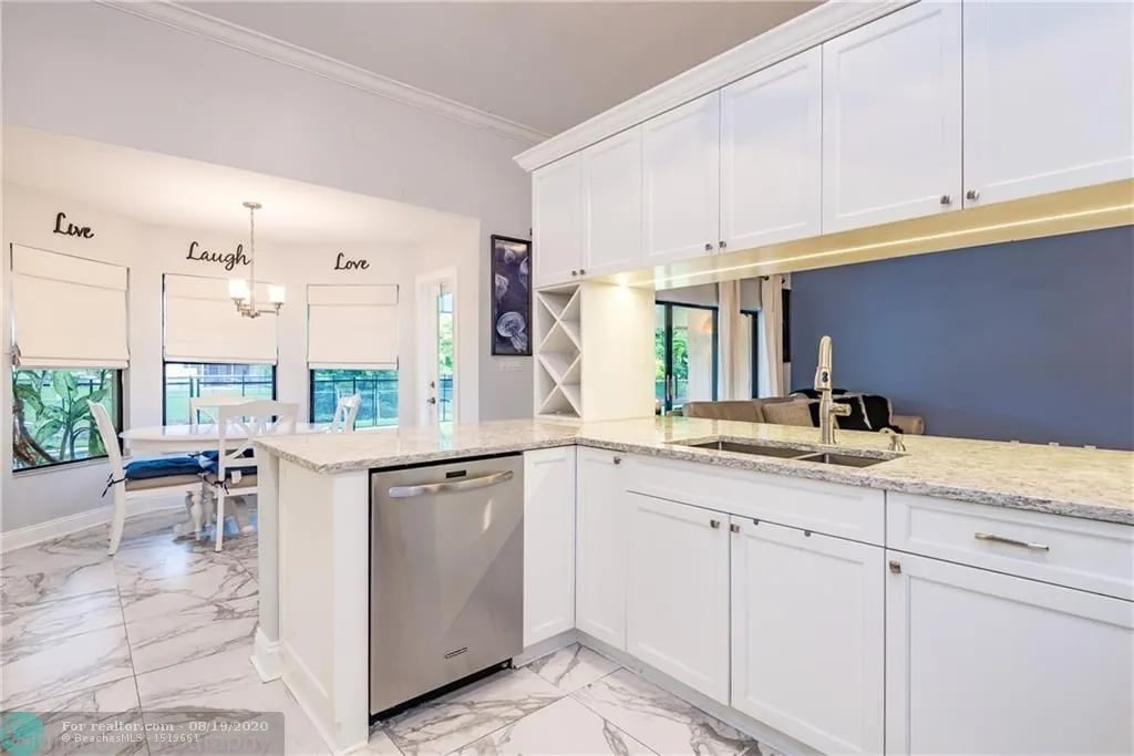 Kitchen with white cabinets, granite island, stainless steel dishwasher, and marble-look tile flooring.