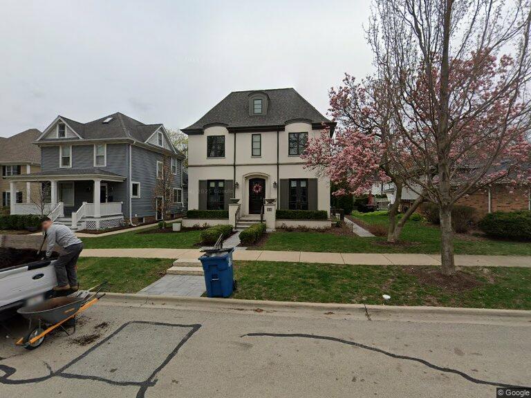 Two-story white house with dark trim, a front porch, and a blooming tree in the yard.