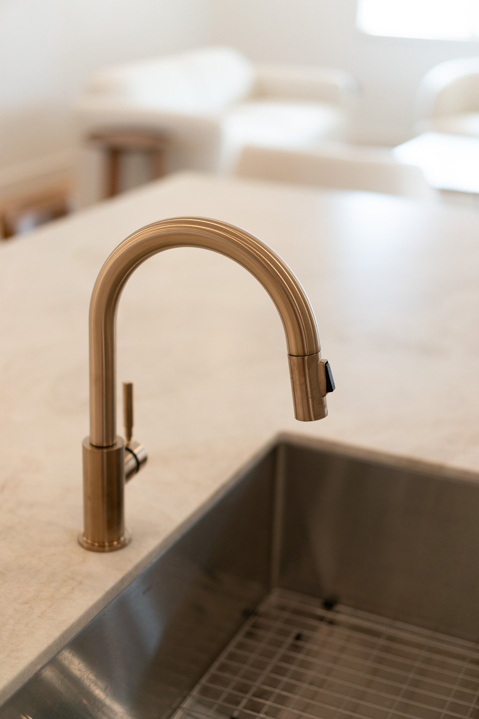 Brass pull-down kitchen faucet over a deep stainless-steel sink and light stone countertop.