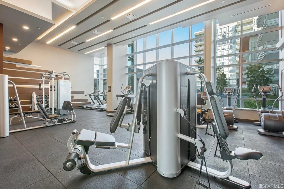 Arden Residences fully equipped fitness center with strength training machines, free weights, and floor-to-ceiling windows overlooking Mission Bay San Francisco