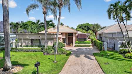 Single-story home with a brick-paver driveway, trimmed hedges, and palm trees along the front lawn.