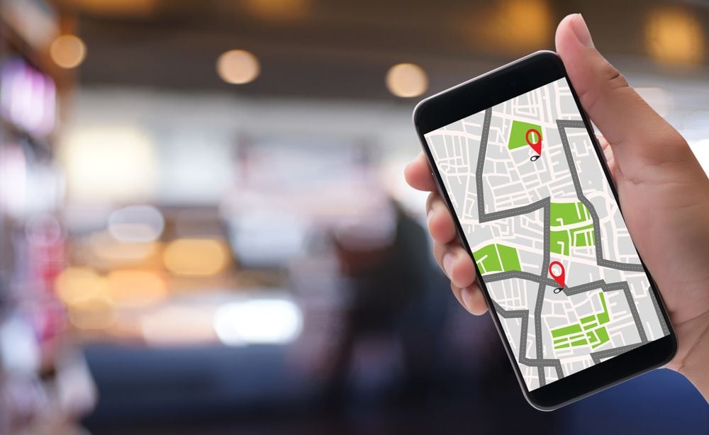 Hand holding a phone with a street map and two location pins.