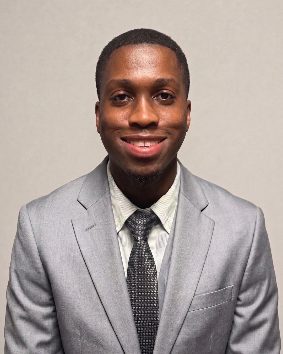 Obed Delvoix smiling in a light gray suit and dark patterned tie.