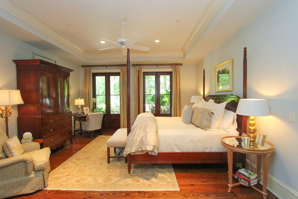 Master bedroom with a dark wood four-poster bed, antique armoire, and tall garden-facing windows.
