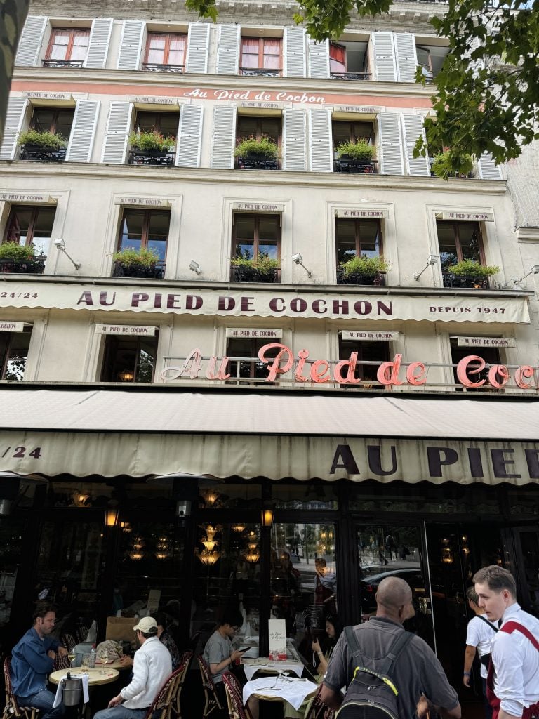Au Pied de Cochon restaurant in Paris, with white shutters, flower boxes, and sidewalk dining.