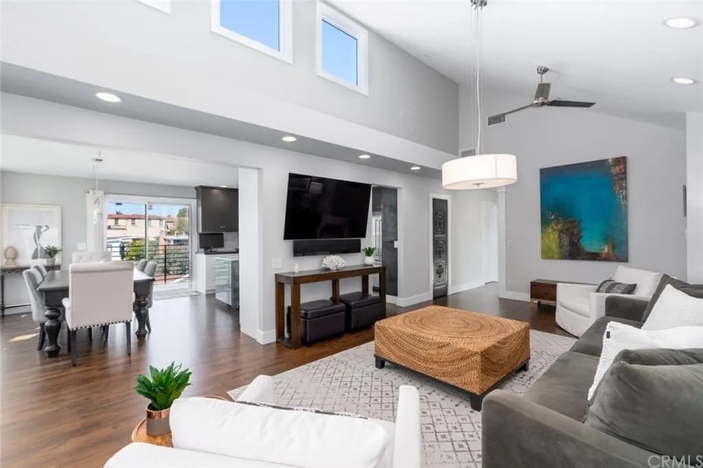  A large open-concept living room with a gray sectional sofa, a woven ottoman, and a flat-screen TV mounted on the wall.