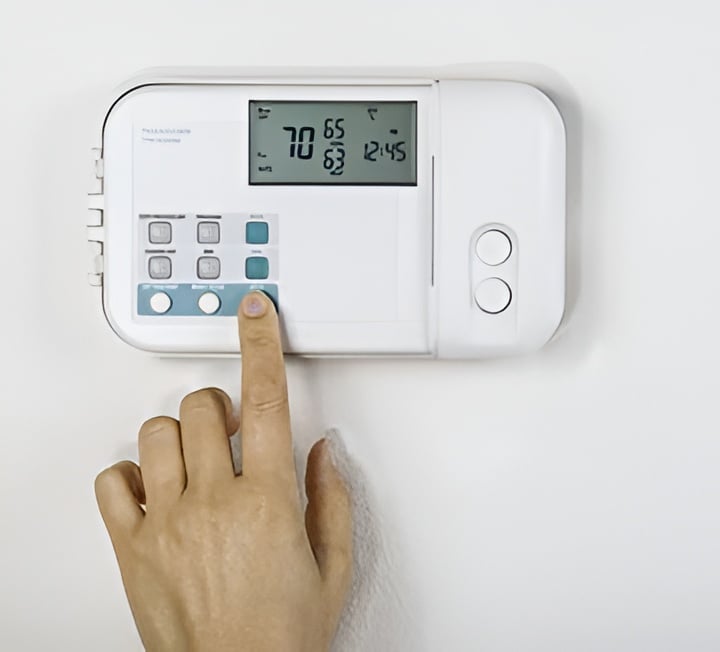 A hand adjusts a wall-mounted digital thermostat.