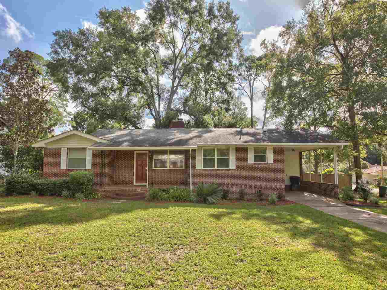 A brick home situated centrally within a spacious yard, surrounded by lush greenery and open space.