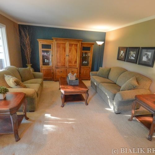 Living room with beige seating, a wooden coffee table, and a large display cabinet against a teal wall.