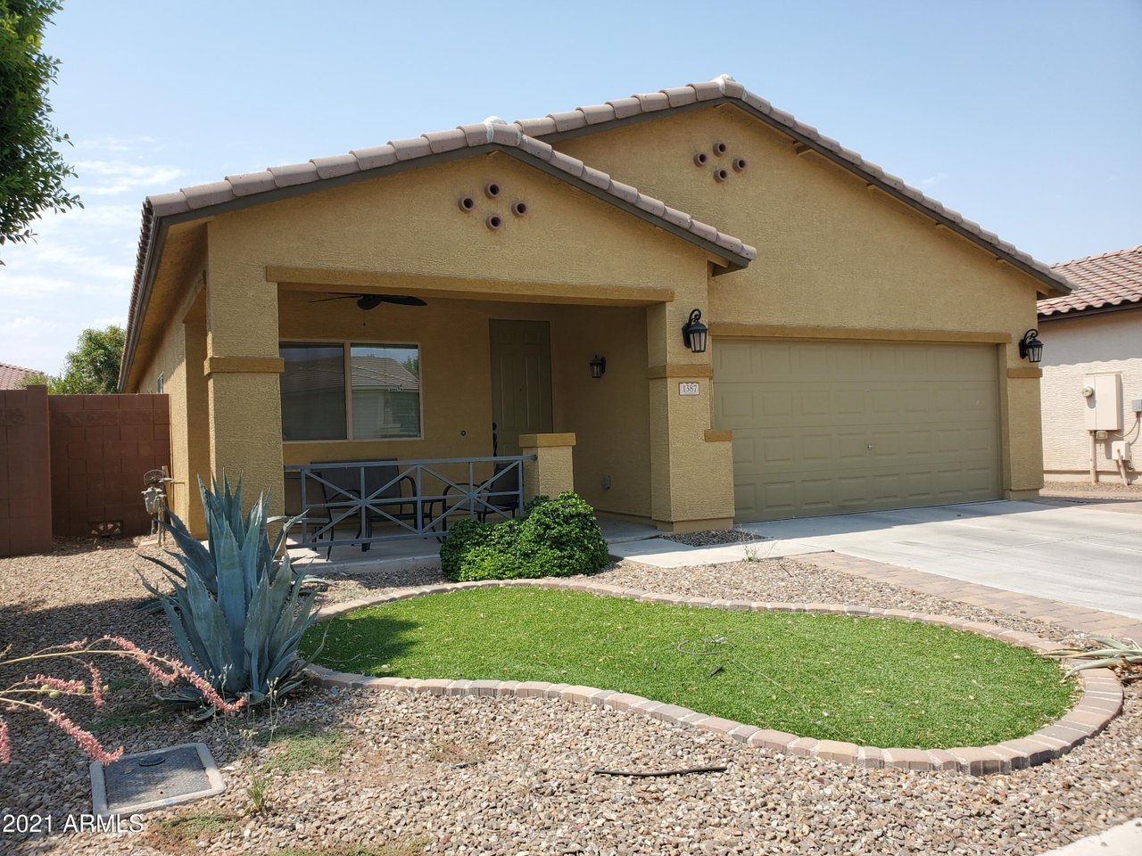 Single-story stucco home with a covered porch, two-car garage, and gravel landscaping.