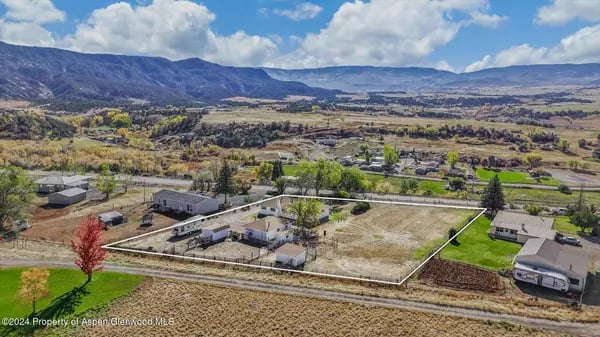 Aerial view of an outlined rural parcel with nearby homes and a mountain backdrop.