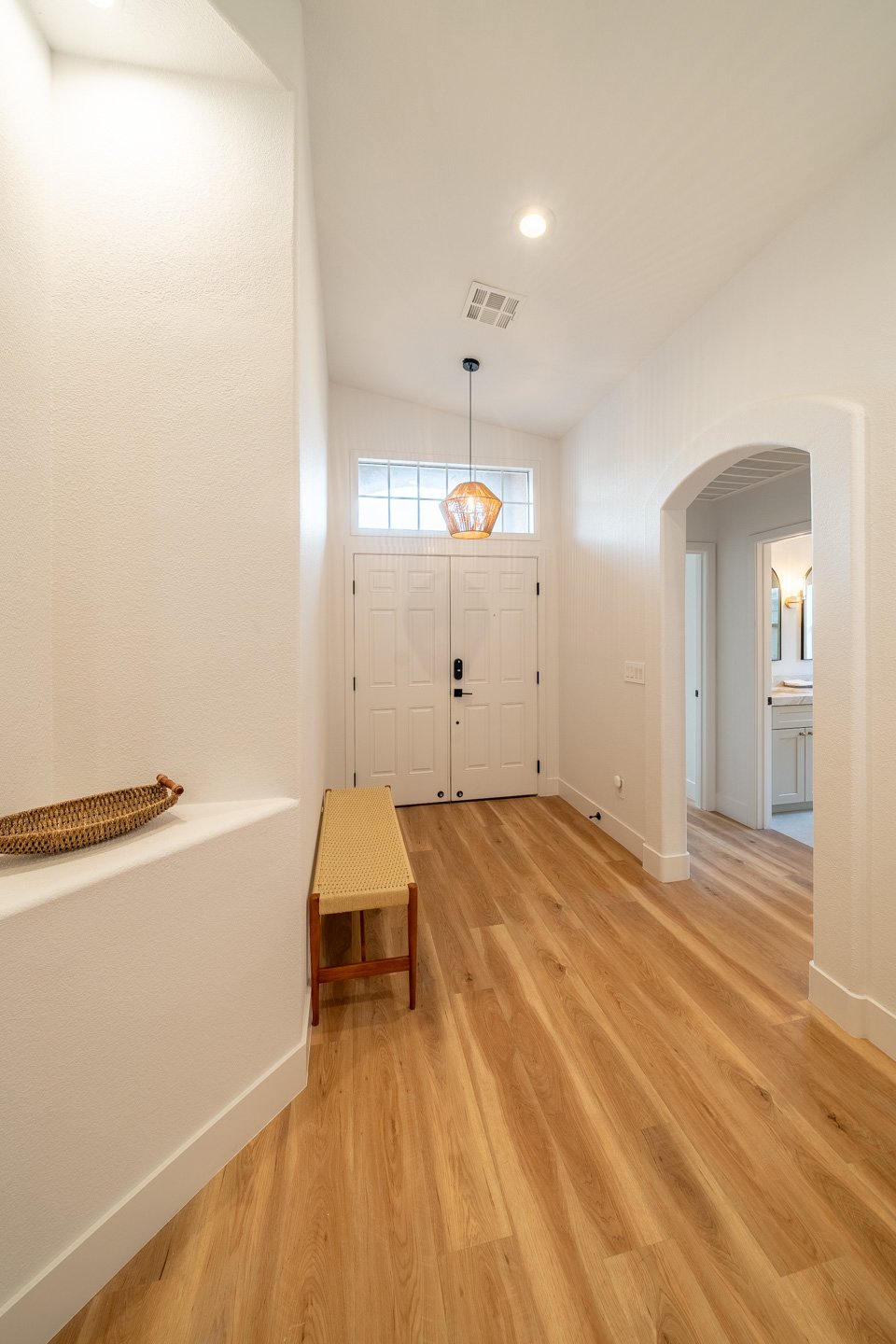 Entry hall with double front doors, a transom window, warm wood floors, and a woven pendant light.