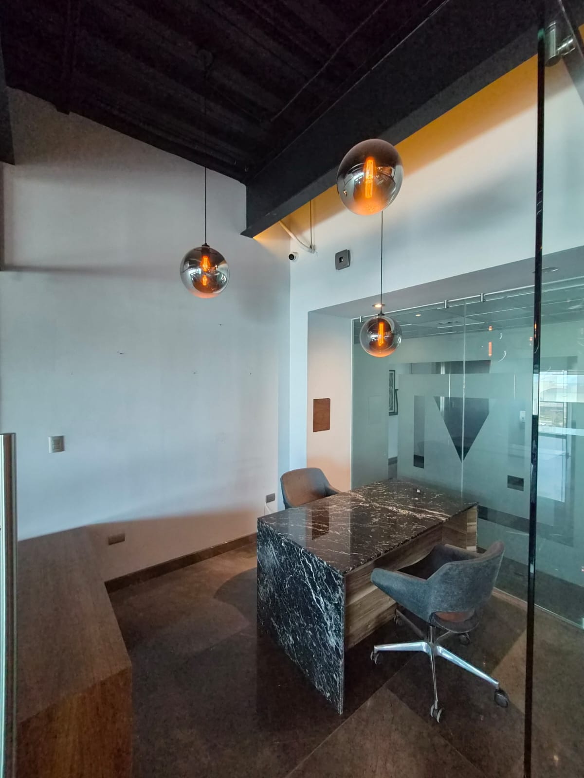 Private office with a marble-and-wood desk, glass partitions, and glowing pendant lights.
