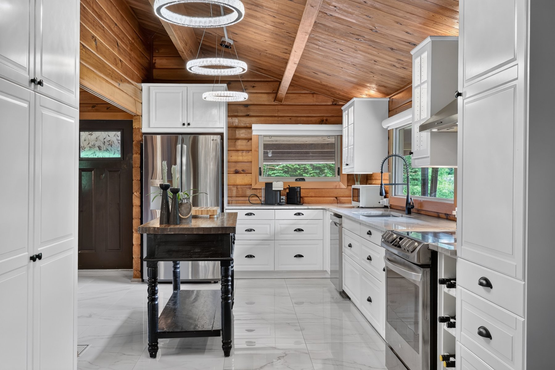 Kitchen with white cabinetry and stainless appliances beneath a vaulted wood-plank ceiling.