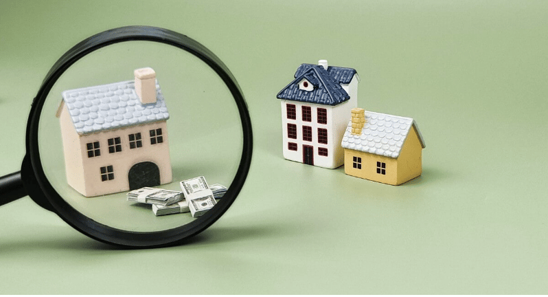 Miniature houses and cash beside a magnifying glass.