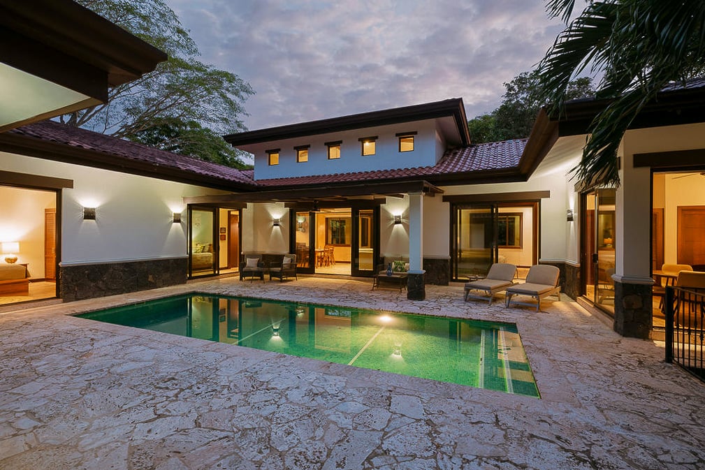 Luxury home courtyard with a swimming pool, stone patio, and warm lights at dusk.