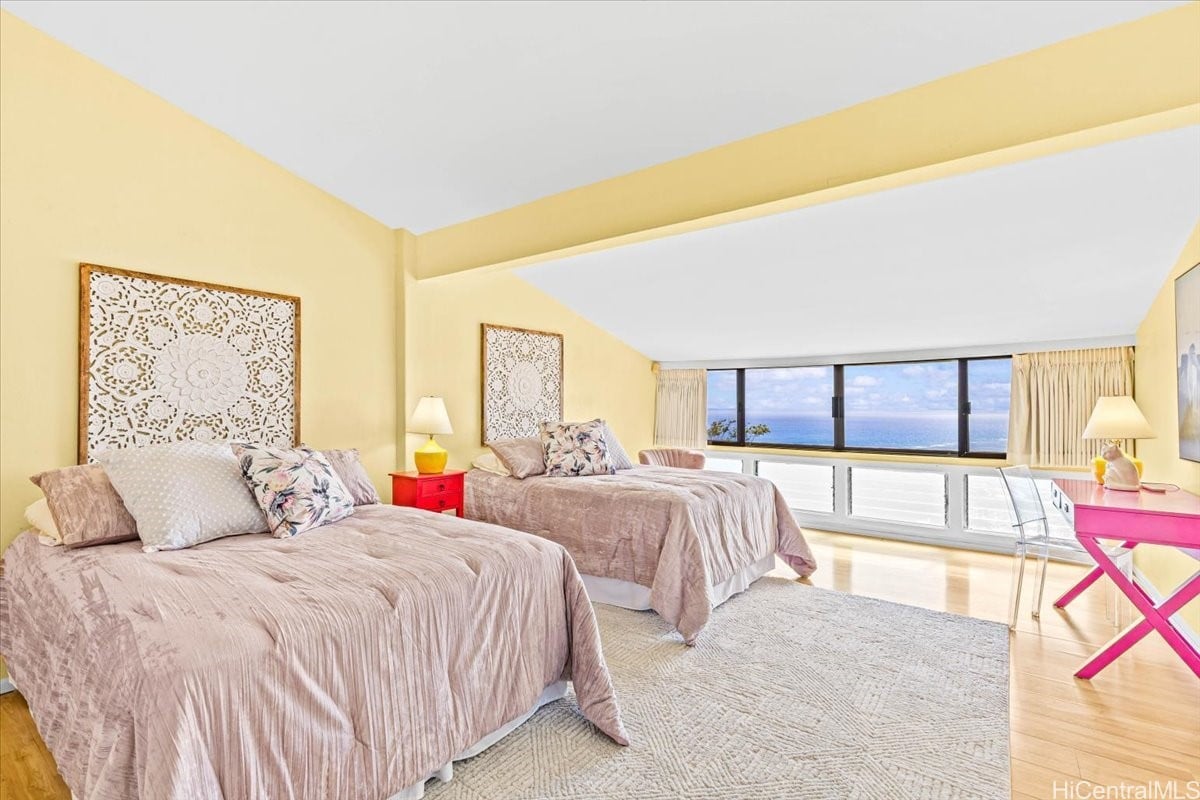 Bedroom with two beds and wide windows overlooking the ocean.