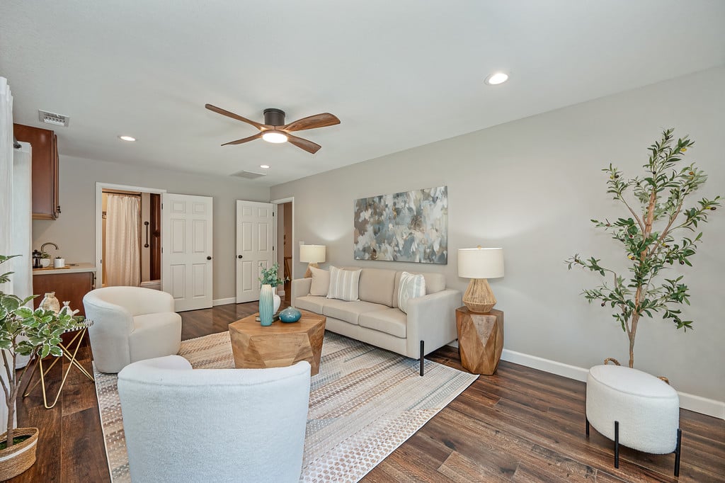 Staged living room with beige seating, dark wood floors, and a ceiling fan.