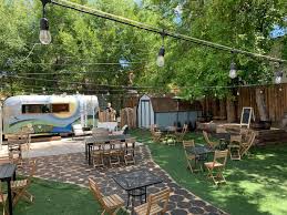 Outdoor restaurant patio with picnic tables, string lights, and a vintage camper.