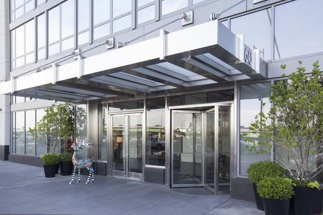 The Aldyn entrance with a white canopy, glass doors, potted shrubs, and a colorful animal sculpture.
