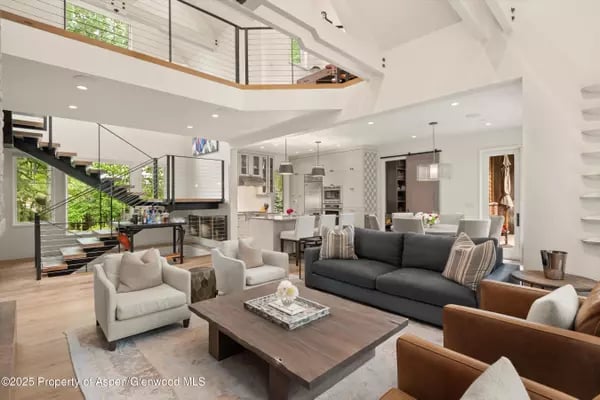 Open-plan living room with a dark gray sofa, kitchen, and black staircase to an upper-level gallery.