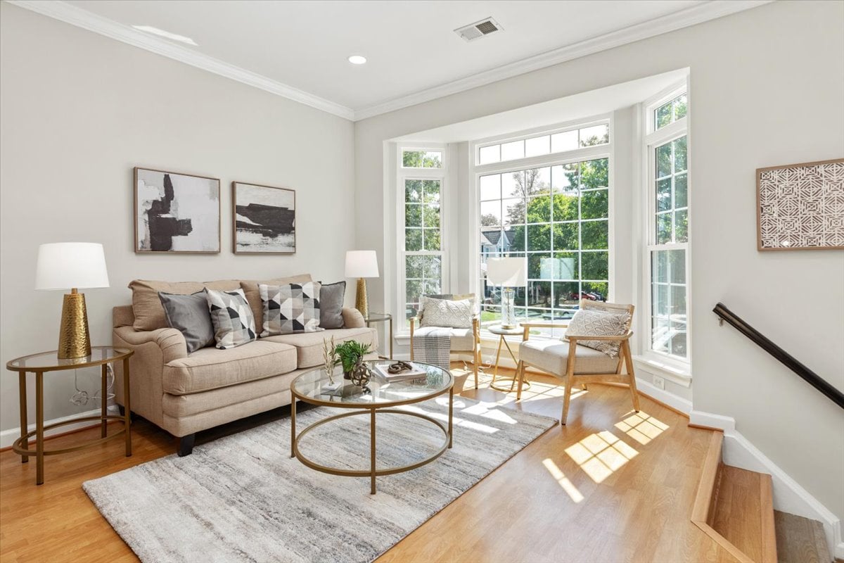 Living room with a beige sofa and chairs beside large sunlit windows.
