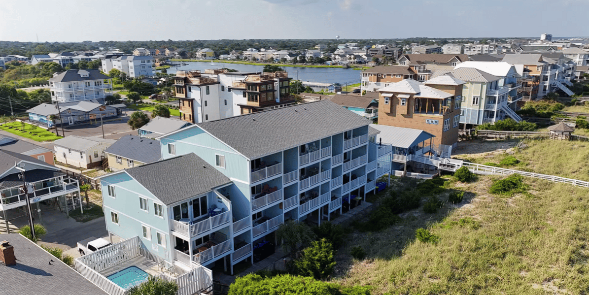 Aerial view of a light-blue condo complex with balconies, a swimming pool, and marsh grass nearby.