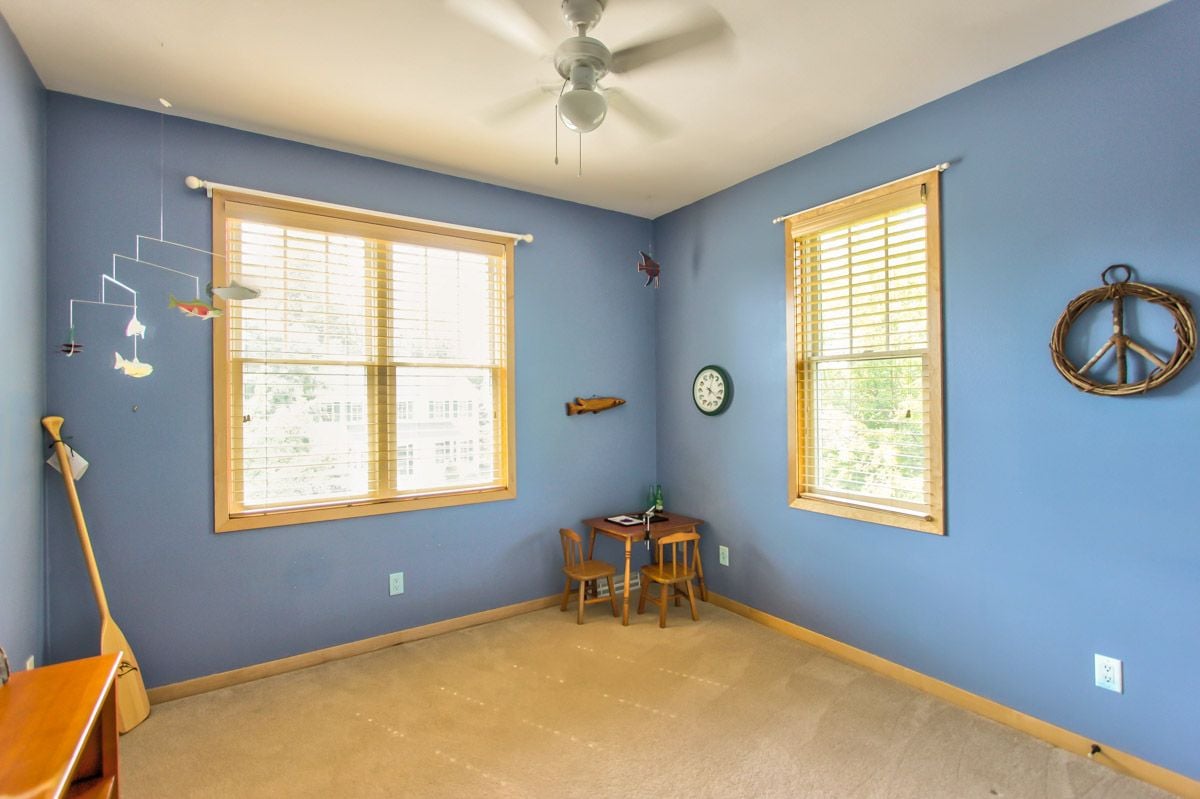Blue room with two sunlit windows, wooden blinds, beige carpet, and a small table with chairs.