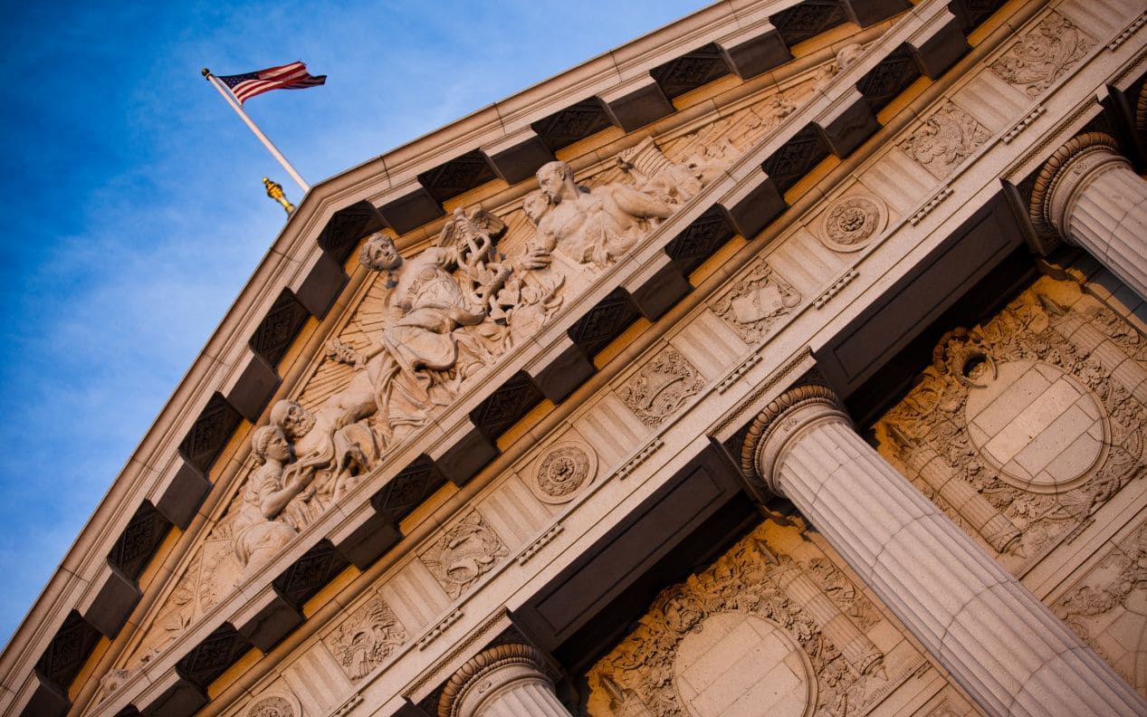 Photo displaying the pediment of San Francisco City Hall, featuring classical sculptures and an American flag flying atop